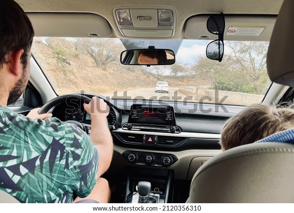 A ride by car. Dad in a T-shirt with a\
tropical print behind the wheel, son\
nearby