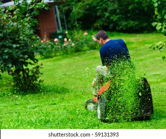 Ride-on lawn mower cutting grass. Focus on grasses in the air