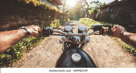 Rider Driving Motorcycle On A Rural Road. Point Of View Shot With Focus Motorbike Handlebar And Man Hands.