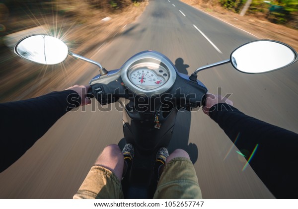 Rider driving scooter on an asphalt\
road. Motion blurred background. First-person\
view