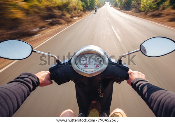 Rider driving scooter on an asphalt\
road. Motion blurred background. First-person\
view