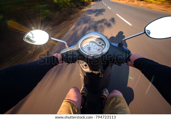 Rider driving scooter on an asphalt
road. Motion blurred background. First-person
view
