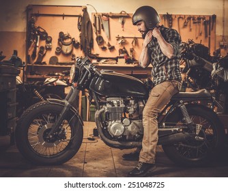 Rider And His Vintage Style Cafe-racer Motorcycle In Customs Garage 