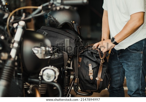 rider install a motorcycle saddlebag or side bag on\
luggage bracket  vintage motorbike. motorcycle travel concept.\
selective focus