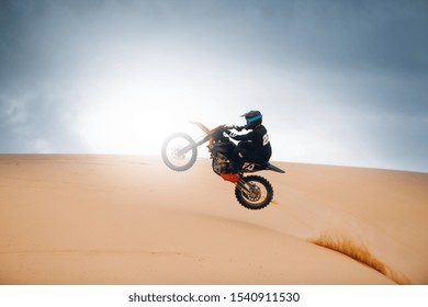 Rider On A Cross-country Motorcycle Jump At The Desert. Dirt Bike Is Jumping Over Dune