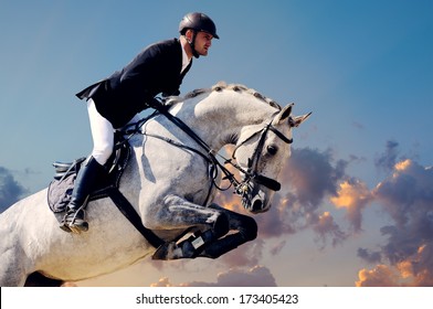Rider on white horse in jump on the background of sunset sky