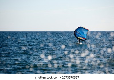 rider with wing foil sails through the sea and splash of water drops jump into the sea