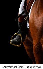 A rider's foot on brown horse looking forward closeup. A woman's horse riding booted foot standing in a gold stirrup of horse saddle isolated on black background. - Shutterstock ID 2083423993