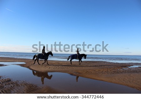 Riders on horses galloping along the shoreline of the ocean.