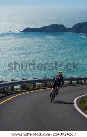Сyclist rides down a mountain road overlooking the Pacific Ocean 