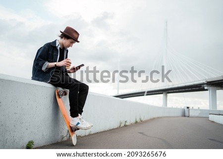 Rides a skateboard in the city and surfs on the phone. Milinal is a young man in a hat and a denim jacket.