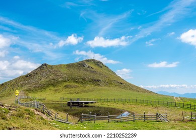 Ridge near green grassy peak of Rindernock (2024m.) and small tarn with wooden deck chairs for sunbathing, beautiful blue sky with white clouds in the background, Nock Mountains, Gurktal Alps, Austria