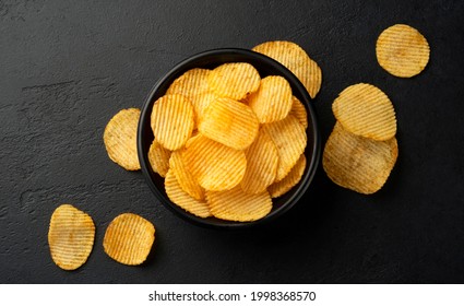 Ridged potato chips in bowl on black background with copy space, top view