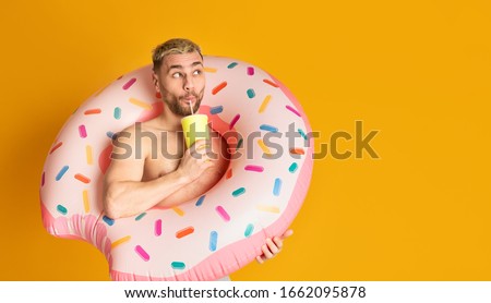Ridiculous guy in inflatable ring, drinking cocktail from straw, empty space