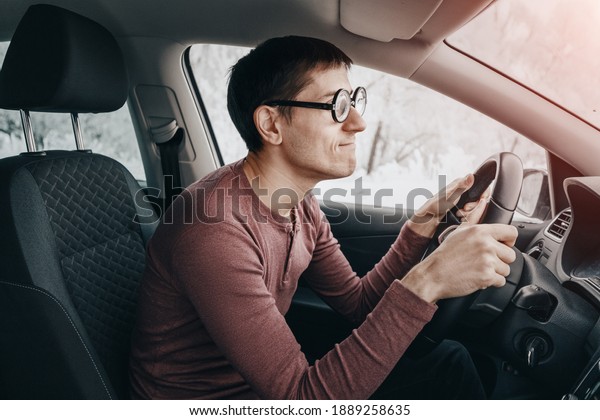 The ridiculous and idiotic nerd\
driver is staring at the road and holding the steering wheel.\
Concept of a novice driver and learning to drive in the\
city