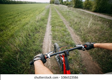 Riding A Bike First Person Perspective With Two Male Hands In Gloves Holding Bicycle Handlebar. Sports, Tourism And Activity Concept