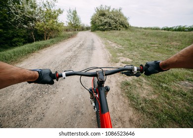 Riding A Bike First Person Perspective With Two Male Hands In Gloves Holding Bicycle Handlebar. Sports, Tourism And Activity Concept