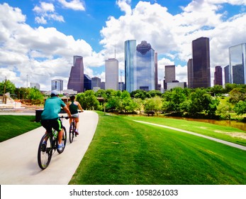 Riding Bikes on Paved Trail in Houston Park (view of river and skyline of downtown Houston) - Houston, Texas, USA 