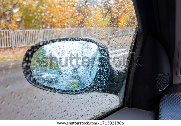 Riding car viewed in the car mirror covered with\
rain drops