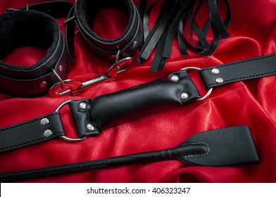 Riding Crop, A Whip Flogger, Leather Handcuffs And A Mouth Gag On Red Satin, Kinky Sex Toys For Dom / Sub Sexual Games And Other Forms Of Kink