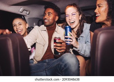 Riding Home With Joy. Group Of Four Happy Friends Laughing Cheerfully While Sitting Together In The Back Seat Of A Car. Carefree Friends Having A Good Time On Their Way Home After A Party.