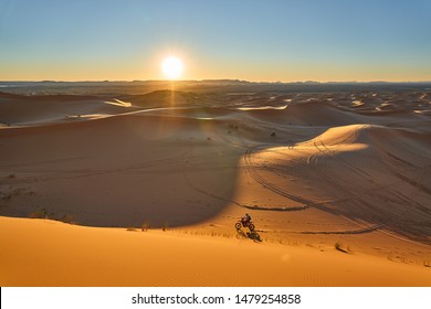 Riding The Motorcycle In The Desert Before Sunset. Sunset Desert Landscape Photo Was Taken In Erg Chebbi Near Merzouga, Saharan Morocco.