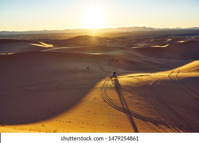 Riding The Motorcycle In The Desert Before Sunset. Sunset Desert Landscape Photo Was Taken In Erg Chebbi Near Merzouga, Saharan Morocco.