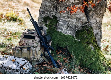 Rifle And Military Camo Backpack Under The Tree