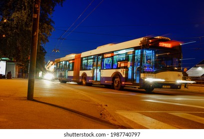 Riga, Latvia 02.06.2021 Long Exposure Night Photo In Which A Blue Bus With Its Headlights On Is Driving Away From The Bus Stop.