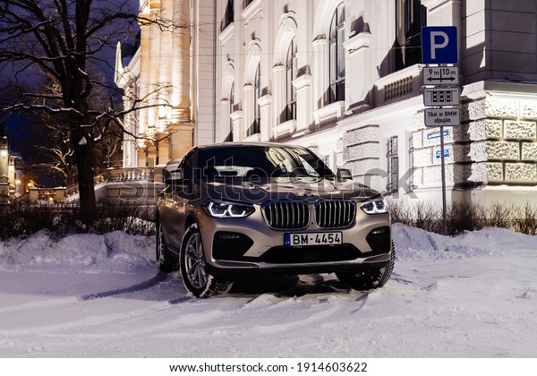 Riga, Latvia 10 February 2021 BMW X4 G02\
stands on parking lot with led light on. Front and side view of the\
car. Background city houses and snowy road.\
