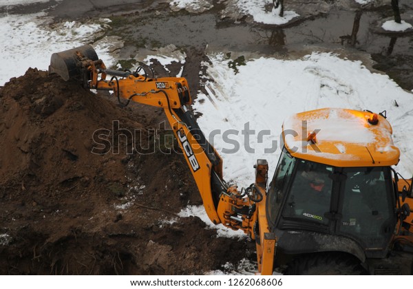 RIGA, LATVIA – 19 DECEMBER,\
2018: Excavator digs a hole. Burst pipes. Winter, snow, block\
houses