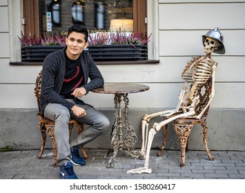 Riga, Latvia - 2019 Skeleton And Man Behind Coffee Table At Street