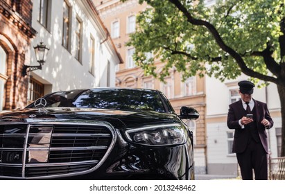 Riga, Latvia 21 July 2021 Limousine Transfer Chauffeur With Chauffeur Hat, Stands By Luxury Car. 
Holding Mobile Phone In Hand. Mercedes Benz S500 S Class W223 