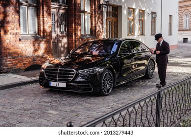 Riga, Latvia 21 July 2021 Limousine Transfer Chauffeur With Chauffeur Hat, Stands By Luxury Car. 
Holding Mobile Phone In Hand. Mercedes Benz S500 AMG S Class W223 