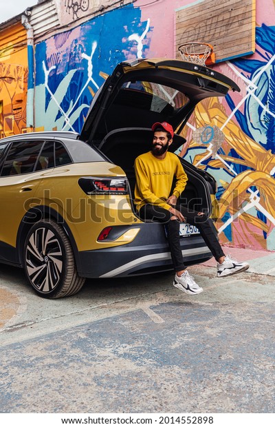 Riga, Latvia 26 July 2021, Volkswagen ID.4 is an\
electric crossover SUV is positioned by Volkswagen as a\
high-volume, mass-market electric vehicle.\
Stands on parking lot\
by graffiti, Man sitting in\
