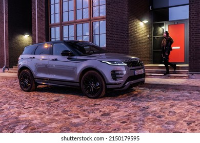 Riga Latvia 27 April 2022, Range Rover Evoque Plug-in Hybrid Brand New Model. Stand On Parking Lot In Modern House Buildings At Night Time, Led Light On. Woman Is Walking To Car