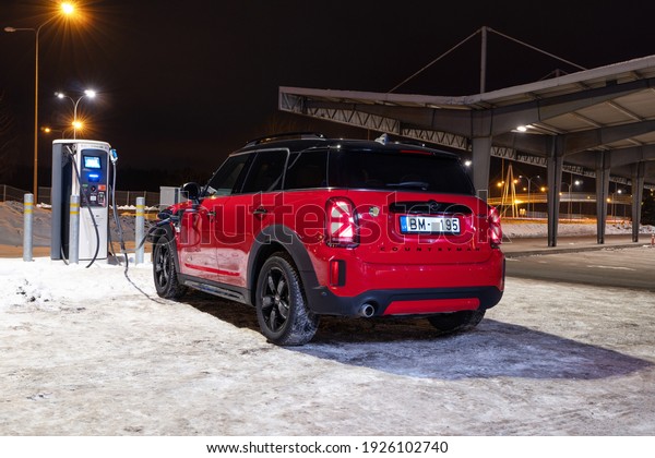 Riga, Latvia 28 February 2021 Mini Cooper S\
Countryman Plug in Hybrid Facelift model stands on parking lot by\
electric charger at night time, Led lights on. MINI John Cooper\
Works package.