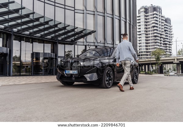Riga Latvia, 4 October 2022, BMW iX i20 M Sport\
mid-size luxury crossover SUV, Black color car stand by Entrance to\
Office House. Sport SUV electric vehicle by BMW. Man walking to\
BMW. Business Man.