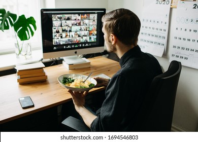 Riga, Latvia - April 04 2020: Man Having Lunch At The Table In Home Office While Having Zoom Video Conference Call Via Computer. Stay At Home And Work From Home Concept During Coronavirus Pandemic