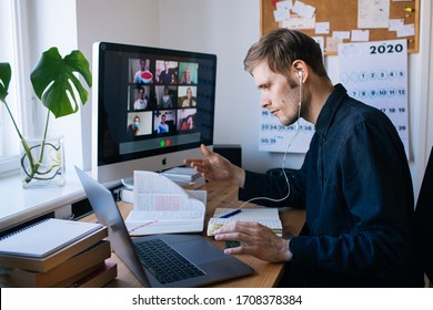 Riga, Latvia - April 19 2020: Virtual Team Meeting Working Remotely From Home With Laptop And Note Book. Side View Of Young Man Making Notes During Virtual Video Chat Conference Call Telecommute