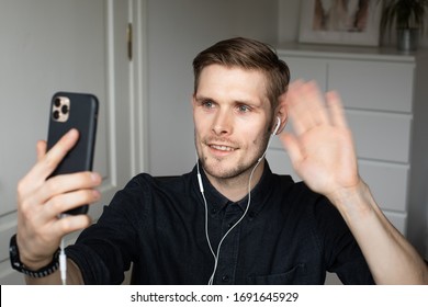 Riga, Latvia - April 2 2020: Young Man Waving To Zoom Video Conference Call Via Smartphone. Home Office. Stay At Home And Work From Home Concept During Coronavirus Pandemic