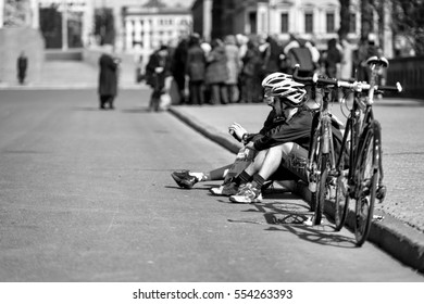 Riga, Latvia - August 14, 2015: Two Unknown Men Sat On The Roadside Alongside Bicycles And Talking.