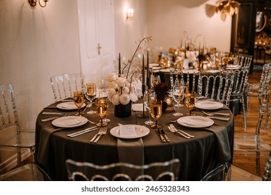 Riga, Latvia, - August 26, 2023 - Elegant indoor wedding reception setting with black tablecloths, white and dark floral centerpieces, gold-rimmed glasses, and clear chairs. - Powered by Shutterstock