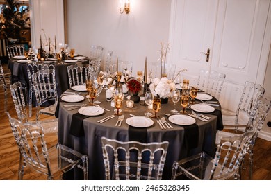 Riga, Latvia, - August 26, 2023 - Sophisticated wedding reception setting featuring black tablecloths, gold-rimmed glassware, floral centerpieces, and clear chairs in an elegant room. - Powered by Shutterstock