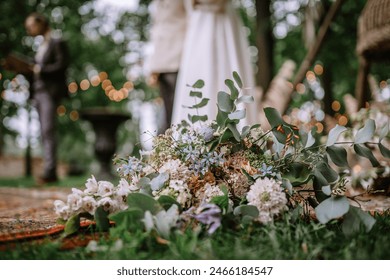 Riga, Latvia, - August 26, 2023 - Close-up of a wedding bouquet on the ground with the blurred bride and groom in the background during their outdoor ceremony. - Powered by Shutterstock