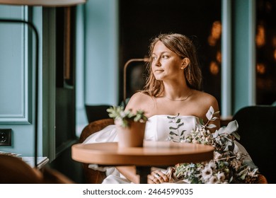 Riga, Latvia, - August 26, 2024 - Bride seated in a cafe, looking thoughtfully out the window, with a bouquet on the table. - Powered by Shutterstock