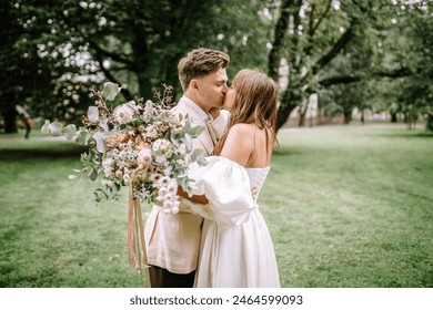 Riga, Latvia, - August 26, 2024 - Bride and groom kissing in park, bride holding large floral bouquet. - Powered by Shutterstock