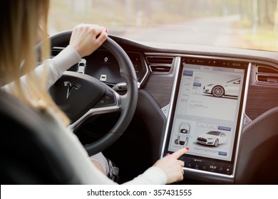 RIGA, LATVIA - DECEMBER 1, 2015: The interior of a Tesla Model S electric vehicle with woman driving and touching its large touchscreen dashboard.