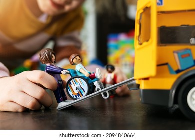 Riga, Latvia - December 22, 2021: Kid Playing With Playmobil Toys On The Floor. School Bus Transportation For Person In Wheelchair. Disability Acceptance Concept