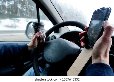 Riga, Latvia, January 02, 2019: A Man Using A Mobile Phone At The Wheel Of A Car  And Drink A Cofee 